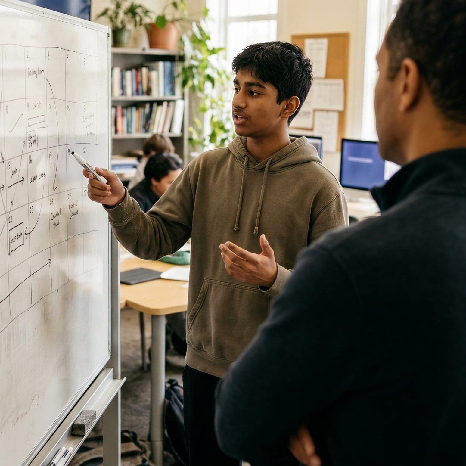 A student points at a weekly plan on a whiteboard while a coach listens.